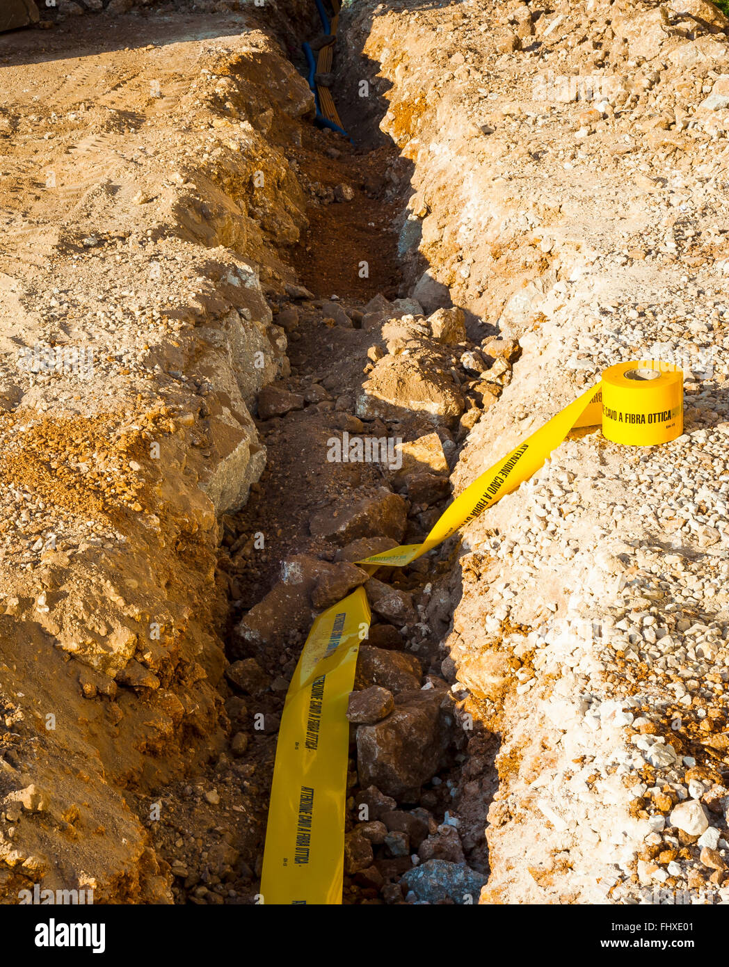 Il posizionamento del nastro di segnalazione posto nelle trincee per individuare un condotto di passaggio per cavi di fibre ottiche. Foto Stock