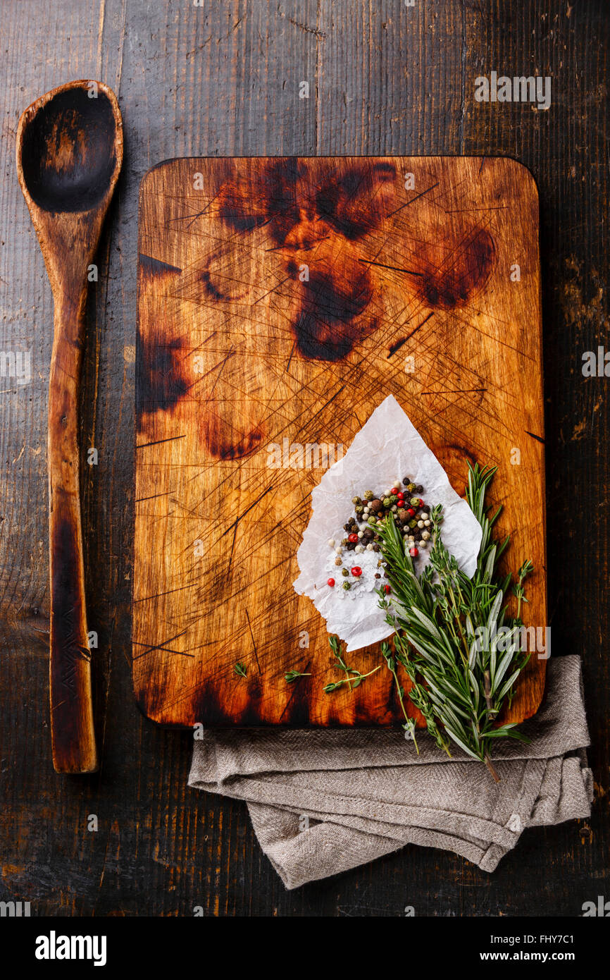Tagliere vecchio cucchiaio di legno condimenti e rosmarino scuro dello sfondo in legno Foto Stock