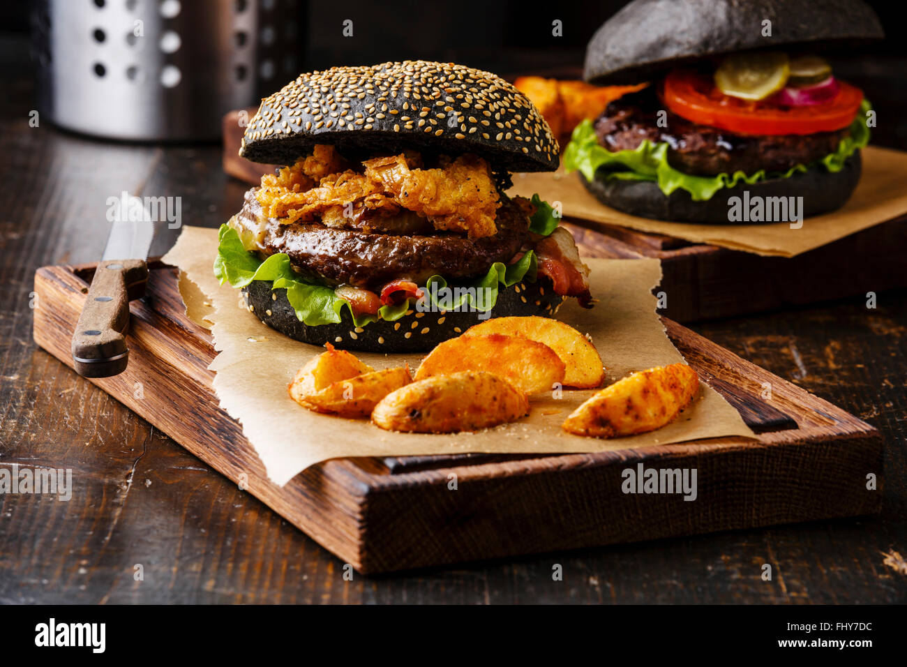 Burger di nero con semi di sesamo bun carne bacon onion patatine fritte e anelli di Spicchi di patate su scuro dello sfondo in legno Foto Stock