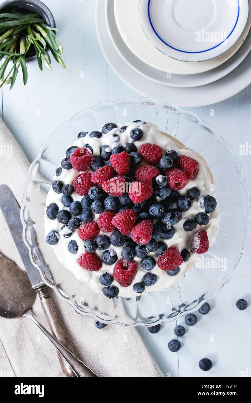 Vintage cake stand con dessert di meringa Pavlova con fresco di more e lamponi. Blu su un tavolo di legno con il vecchio tablew Foto Stock