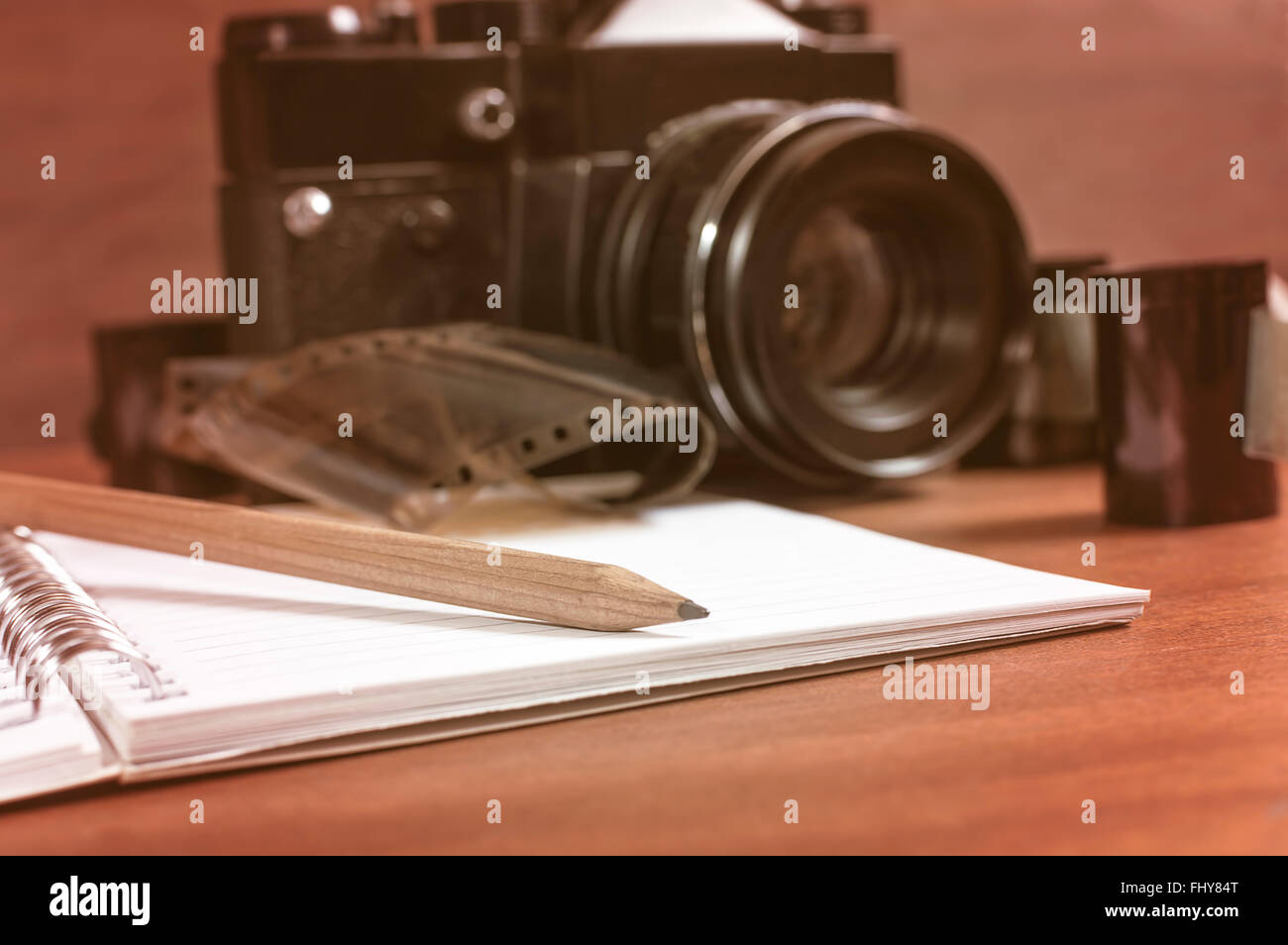 Vecchia fotocamera reflex sul tavolo accanto al negativo la striscia del film e in primo piano un notebook e una matita. Il fuoco selettivo sulla matita. Foto Stock