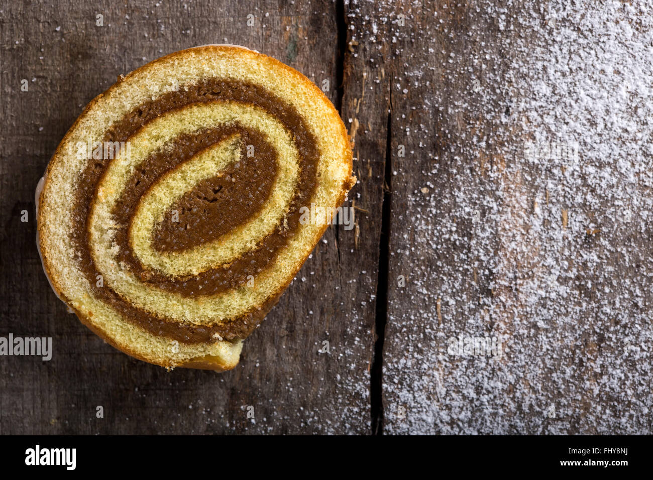 Rotolo di cioccolato torta con caramello e salsa alla vaniglia su sfondo di legno con copia spazio e polvere di zucchero Foto Stock
