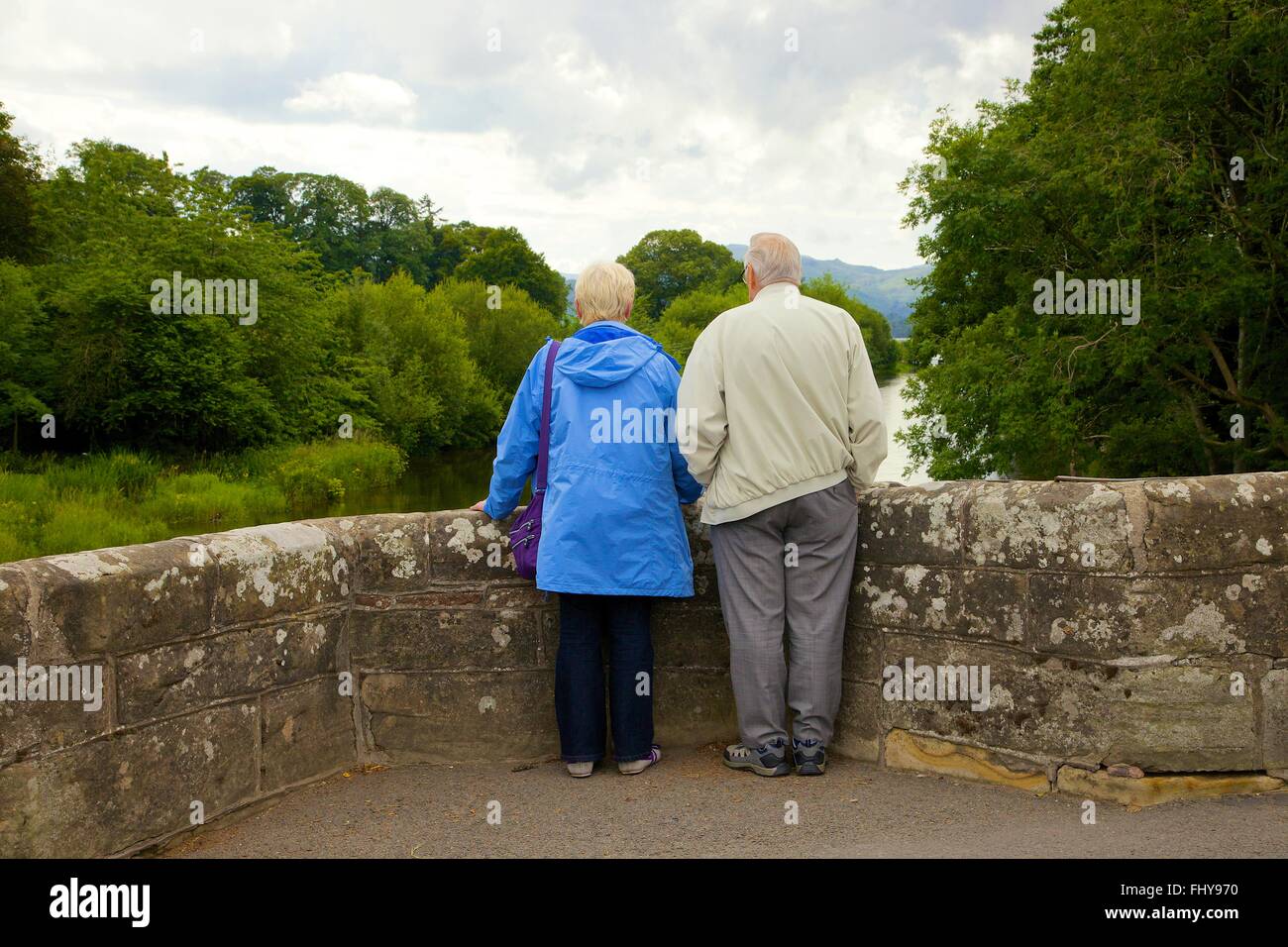 Coppia in pensione in piedi sul parapetto di ponte, godendo della vista. Pooley Bridge, Parco Nazionale del Distretto dei Laghi, Eden District, Cumbria Foto Stock
