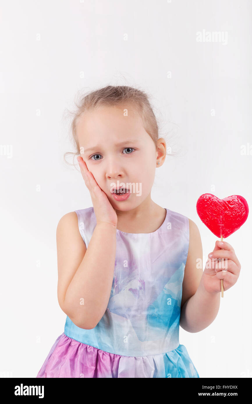 Il mal di denti. Bambina con lecca-lecca e ferire i denti tenendo la sua guancia. Foto Stock