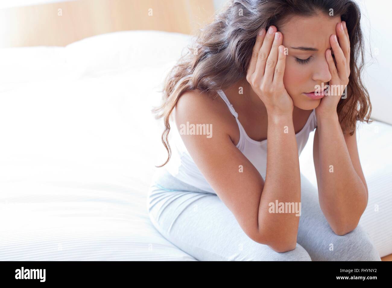 Modello rilasciato. Donna seduta sul letto di toccare la sua testa e la faccia del dolore. Foto Stock