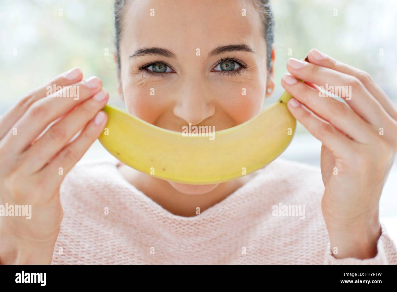 Modello rilasciato. Metà donna adulta tenendo una banana davanti al suo volto. Foto Stock