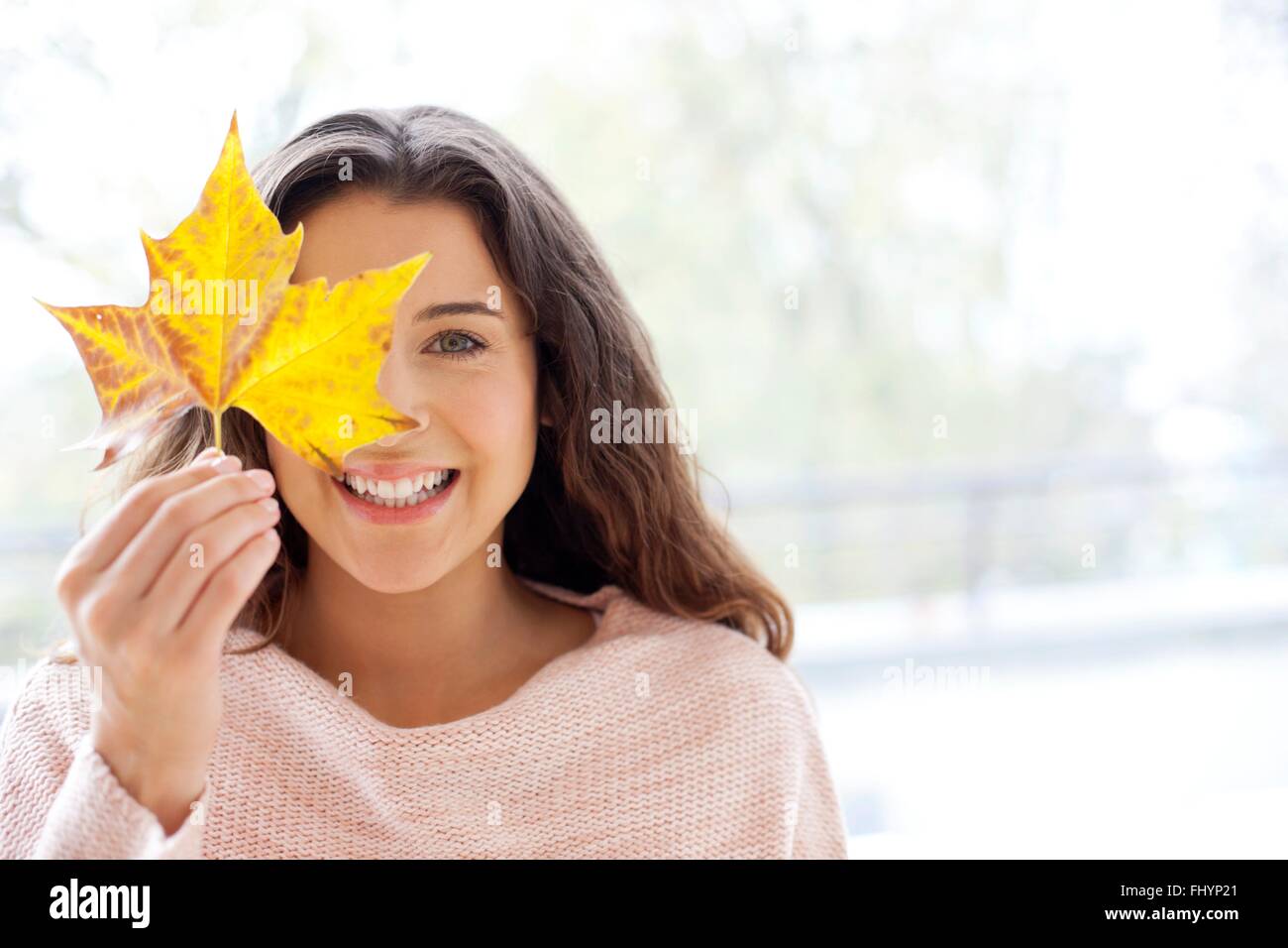 Modello rilasciato. Metà donna adulta tenendo un autunno foglia nella parte anteriore del suo volto. Foto Stock