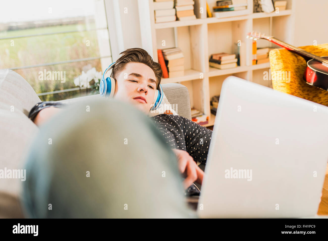 Giovane uomo disteso sul lettino usando il laptop e le cuffie Foto Stock