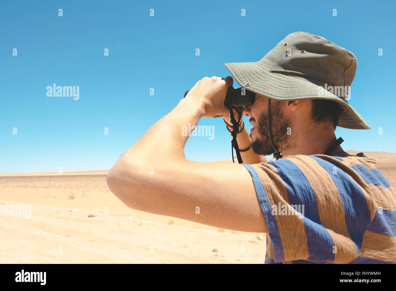 La Namibia, Namib Desert, uomo con hat usando il binocolo per guardare  lontano Foto stock - Alamy