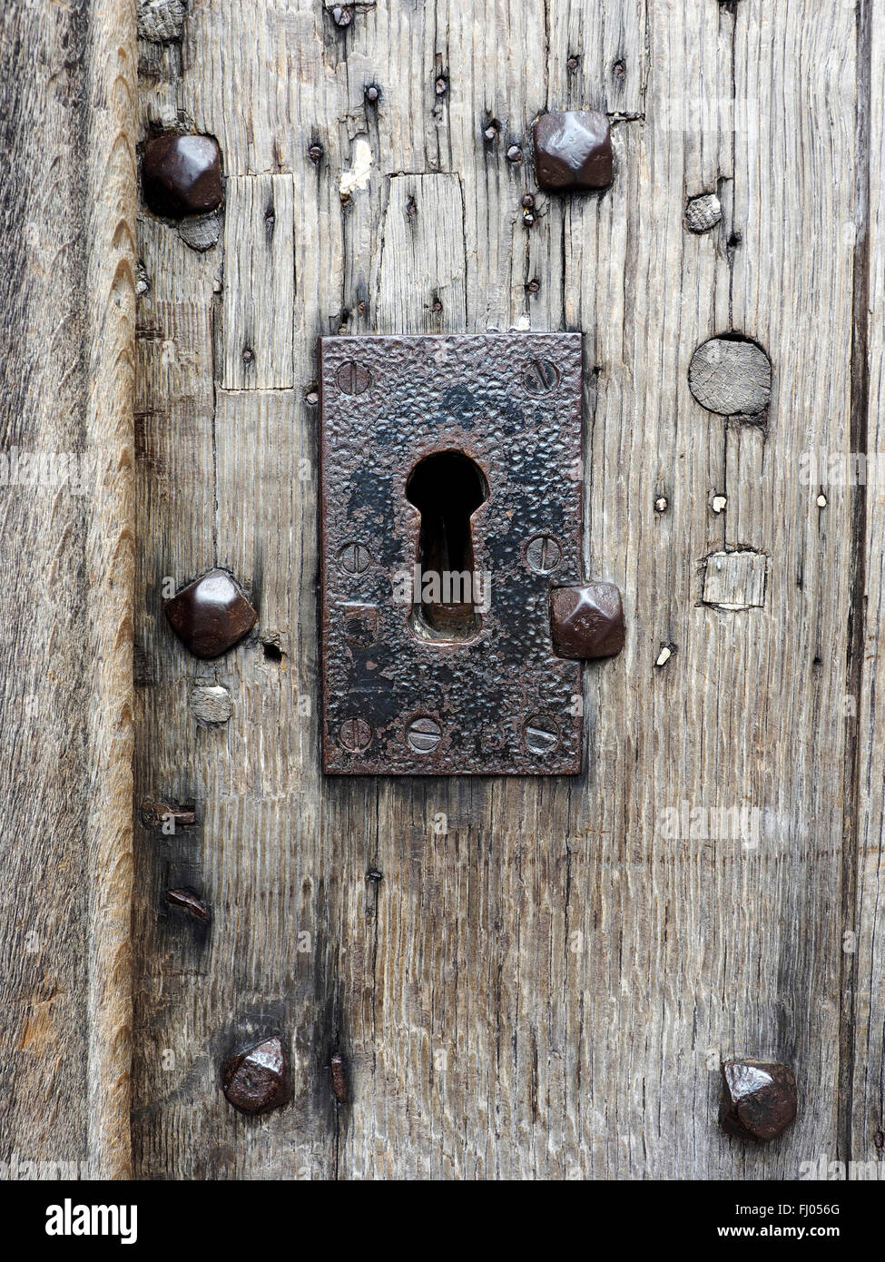 Ferro di grandi dimensioni piastra di rivestimento su una toppa in un antica porta in legno di quercia che mostra le riparazioni e grandi chiodi di ferro. Foto Stock