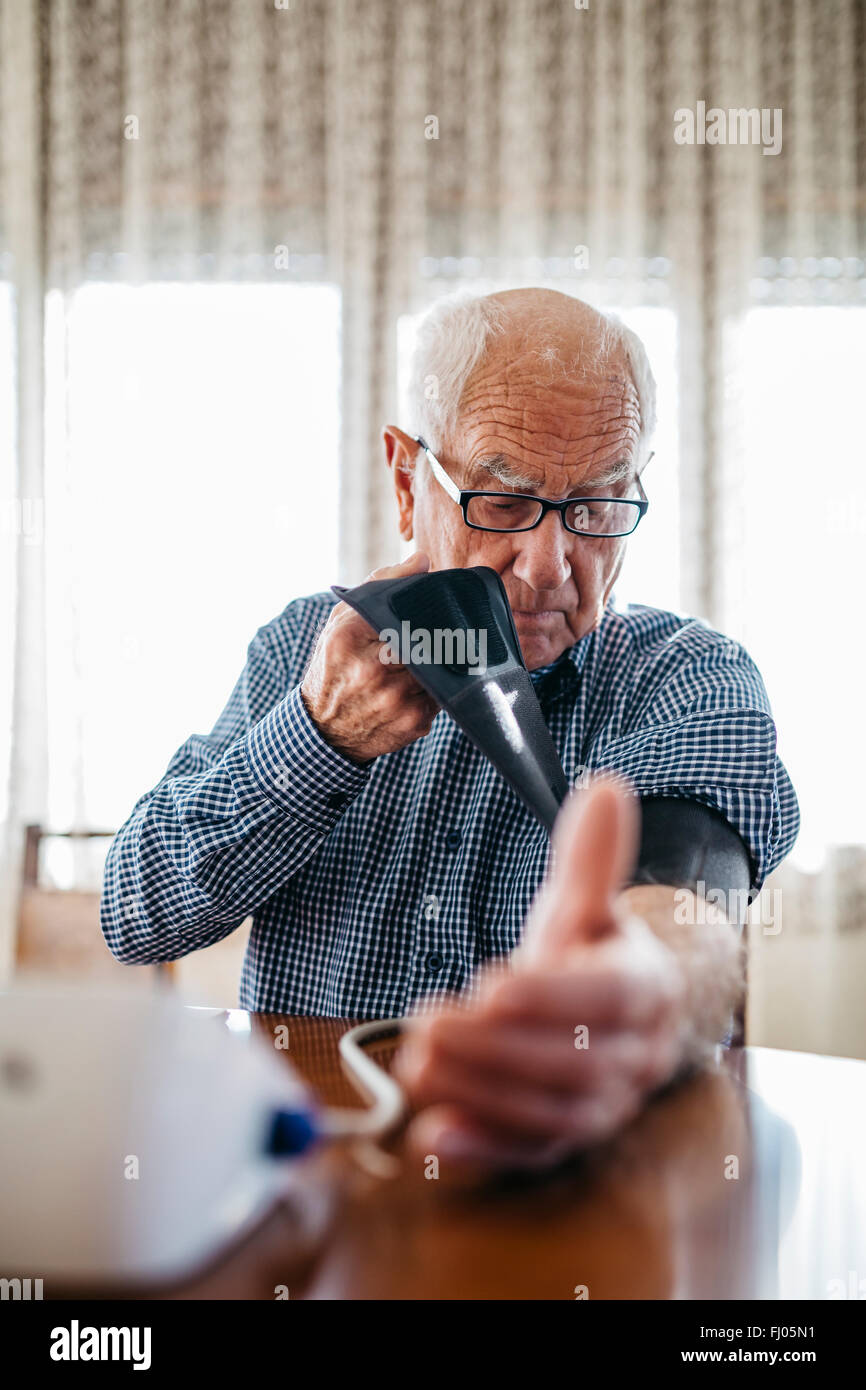 Uomo senior di controllare la sua pressione del sangue a casa Foto Stock