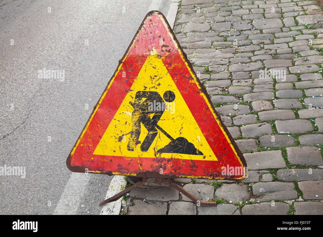 Triangolo rosso e giallo cartello stradale su strada urbana. Gli uomini al lavoro, su strada in costruzione Foto Stock