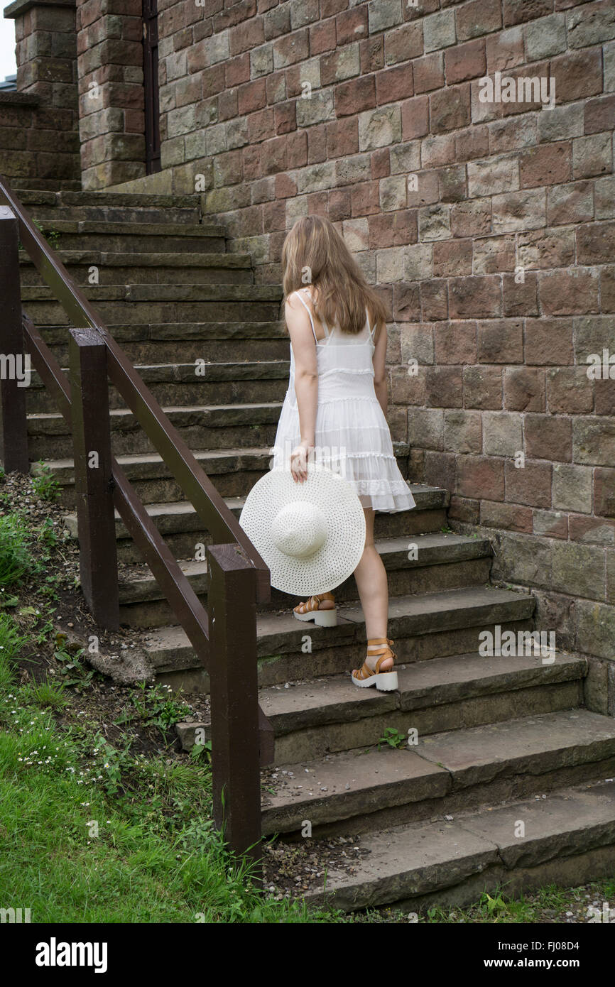Donna in abito bianco tenendo un hat salendo su per le scale fino all'aperto Foto Stock