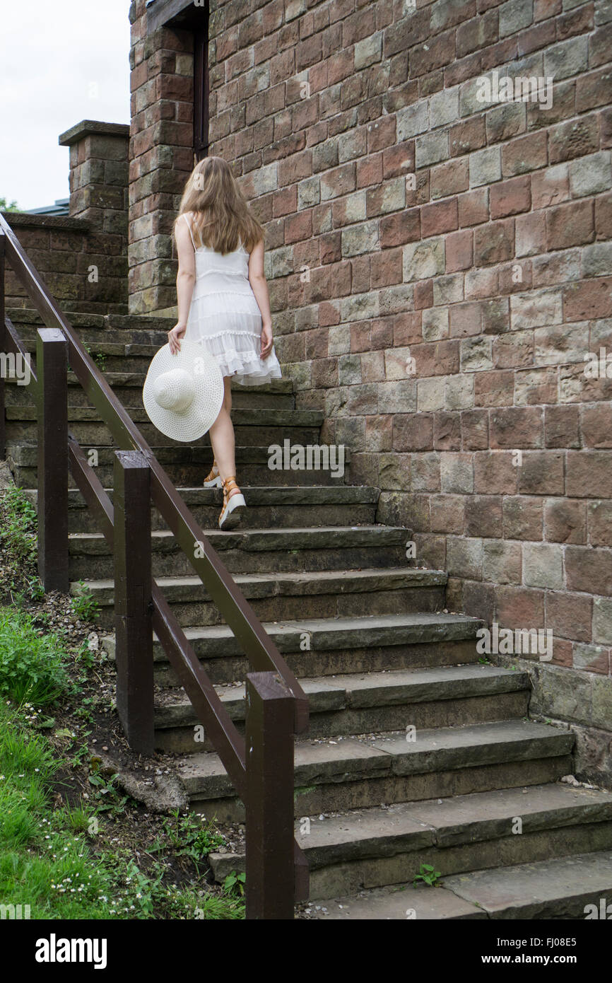 Donna in abito bianco tenendo un hat salendo su per le scale fino all'aperto Foto Stock