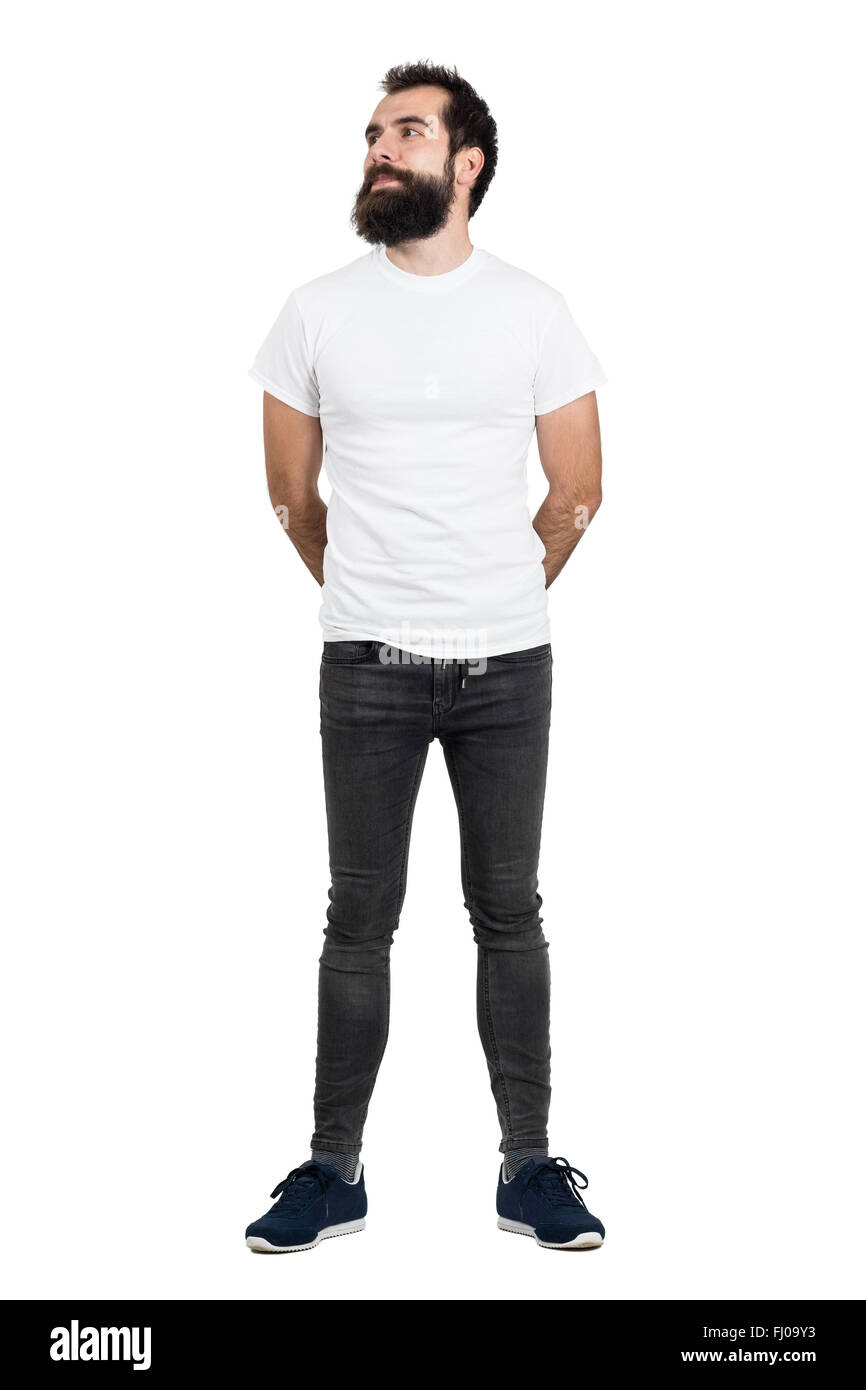 Sorridente uomo barbuto che indossa t-shirt bianca e jeans stretti che guarda lontano. Corpo pieno lunghezza ritratto isolate su sfondo bianco Foto Stock