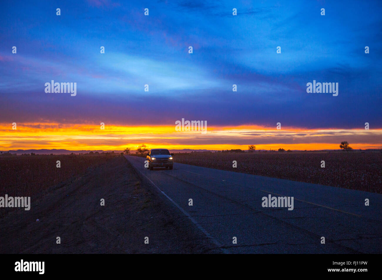 Un auto corre sulla strada nel deserto sotto il rosso scuro e il blu del cielo. È così solo. Dove è la fine ? Foto Stock