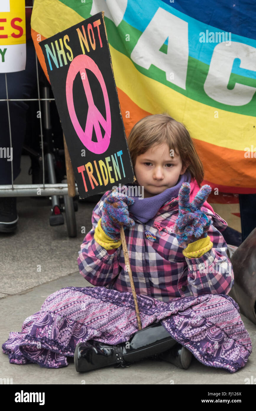 Londra, Regno Unito. Il 27 febbraio 2016. Una ragazza si siede con una targhetta "NHS non Trident" durante gli interventi in contrasto con la spesa di un importo stimato in € 180 miliardi di euro o di più sul rinnovamento di Trident che ha licenziato come fuori della data, totalmente irrilevante per la nostra difesa e un completo spreco di denaro che potrebbe essere messo a molto meglio utilizzare fornendo un adeguato di posti di lavoro e servizi. Peter Marshall, Alamy Live News Foto Stock