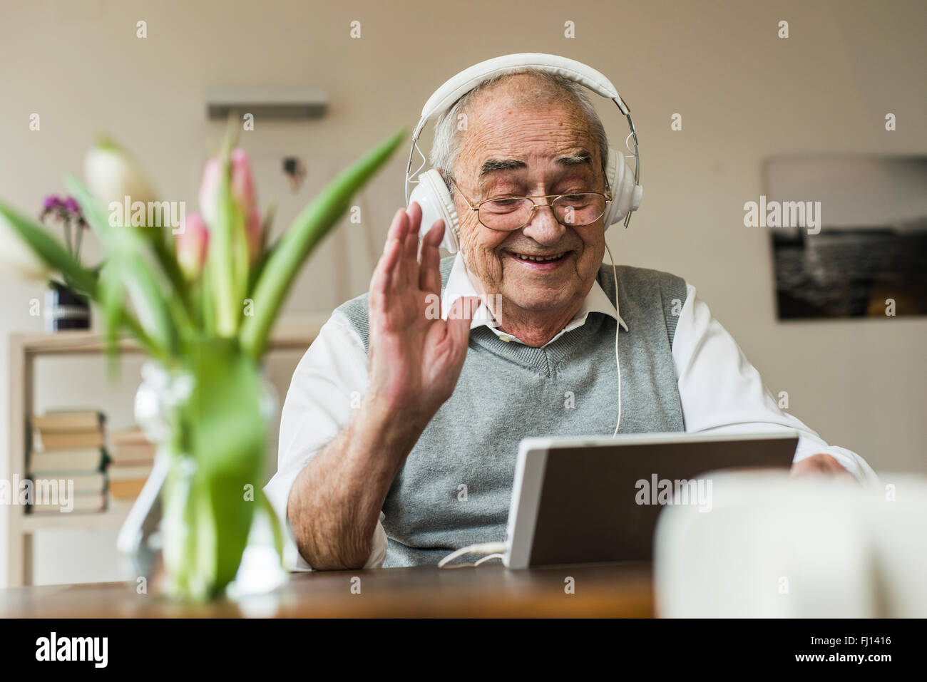 Senior uomo utilizzando mini tablet e cuffie per skyping a casa Foto Stock