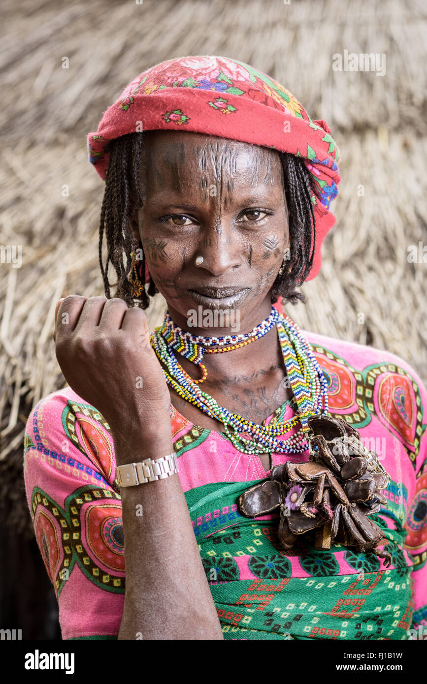 Ritratto di una donna Mbororo con cicatrici sul suo viso e molti buona fortuna amuleti intorno al collo al di fuori del suo rifugio. Foto Stock