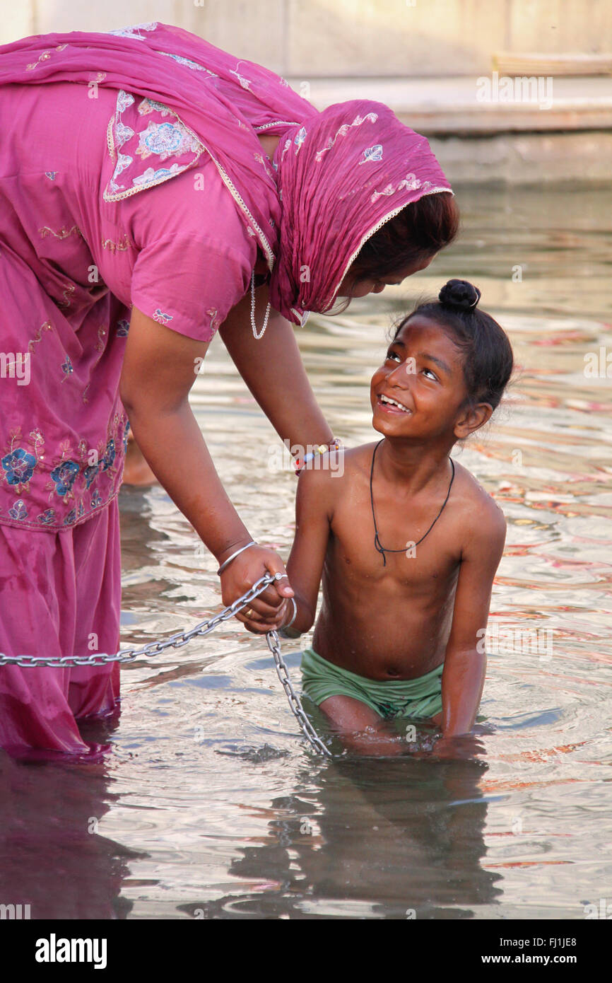 Una madre detiene il suo bambino mentre egli entra nel lago santo del tempio d'oro, Amritsar , India Foto Stock