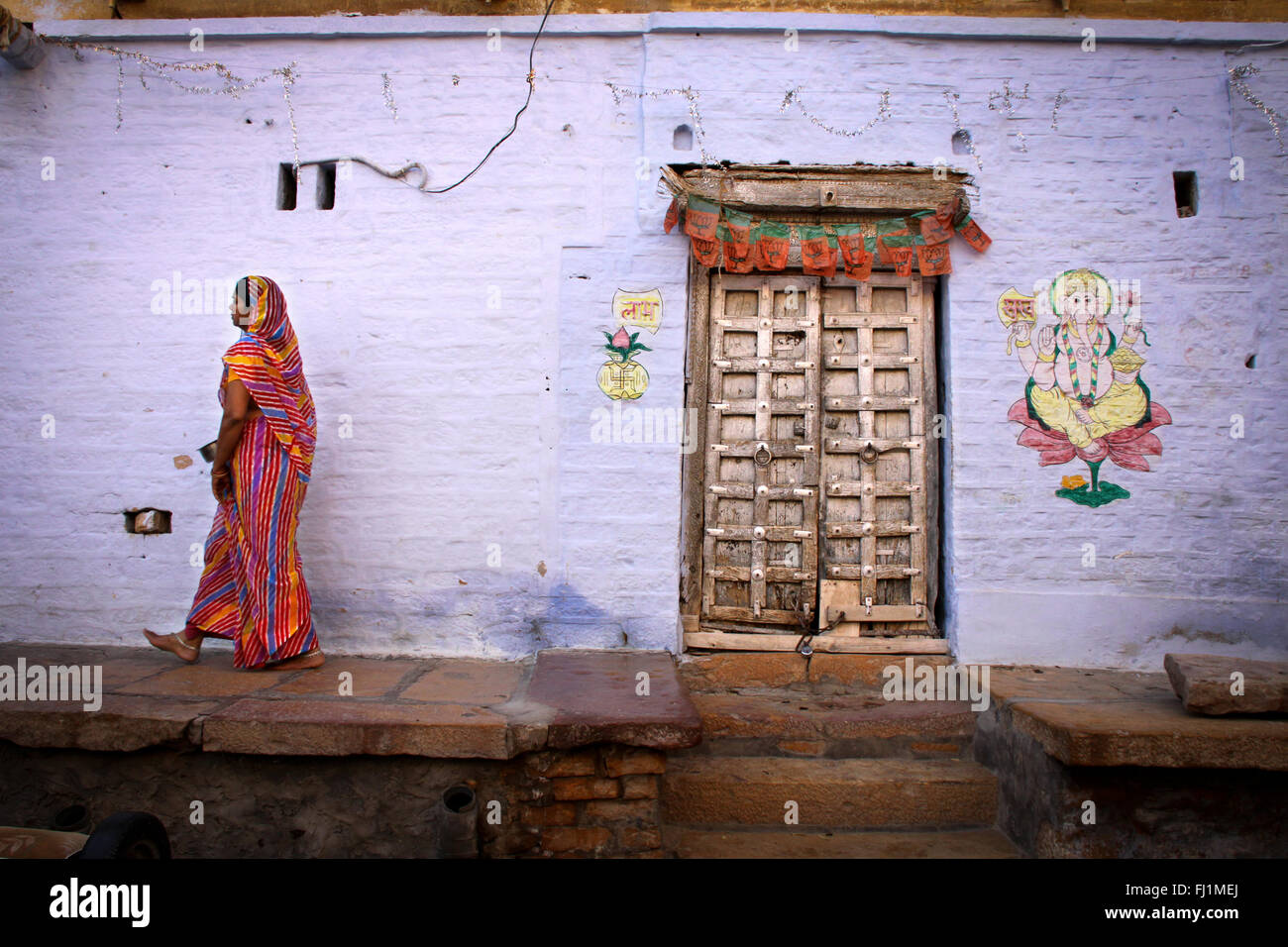 Donna cammina dentro Jaisalmer fort, di fronte a una casa con Lord Ganesh pittura, Rajasthan, India Foto Stock