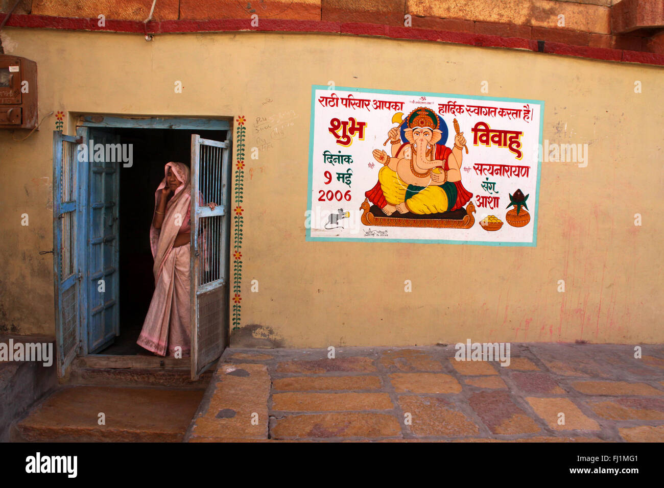 Una donna si trova all'ingresso di una casa in Jaisalmer fort, con la pittura di dio indù Ganesh sulla parete , Jaisalmer , India Foto Stock