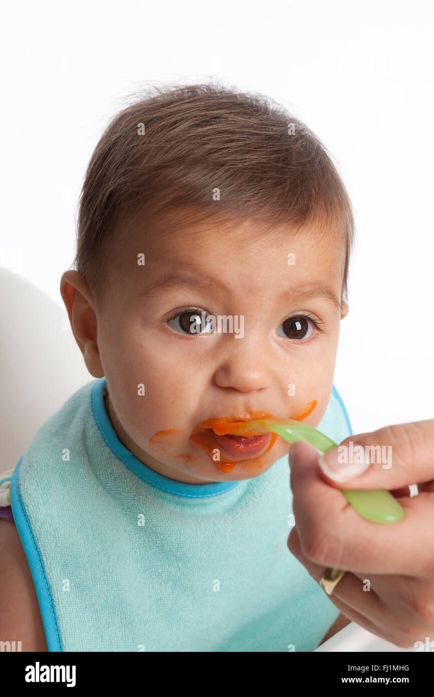 Baby girl è mangiare le carote con un cucchiaio su sfondo bianco Foto Stock