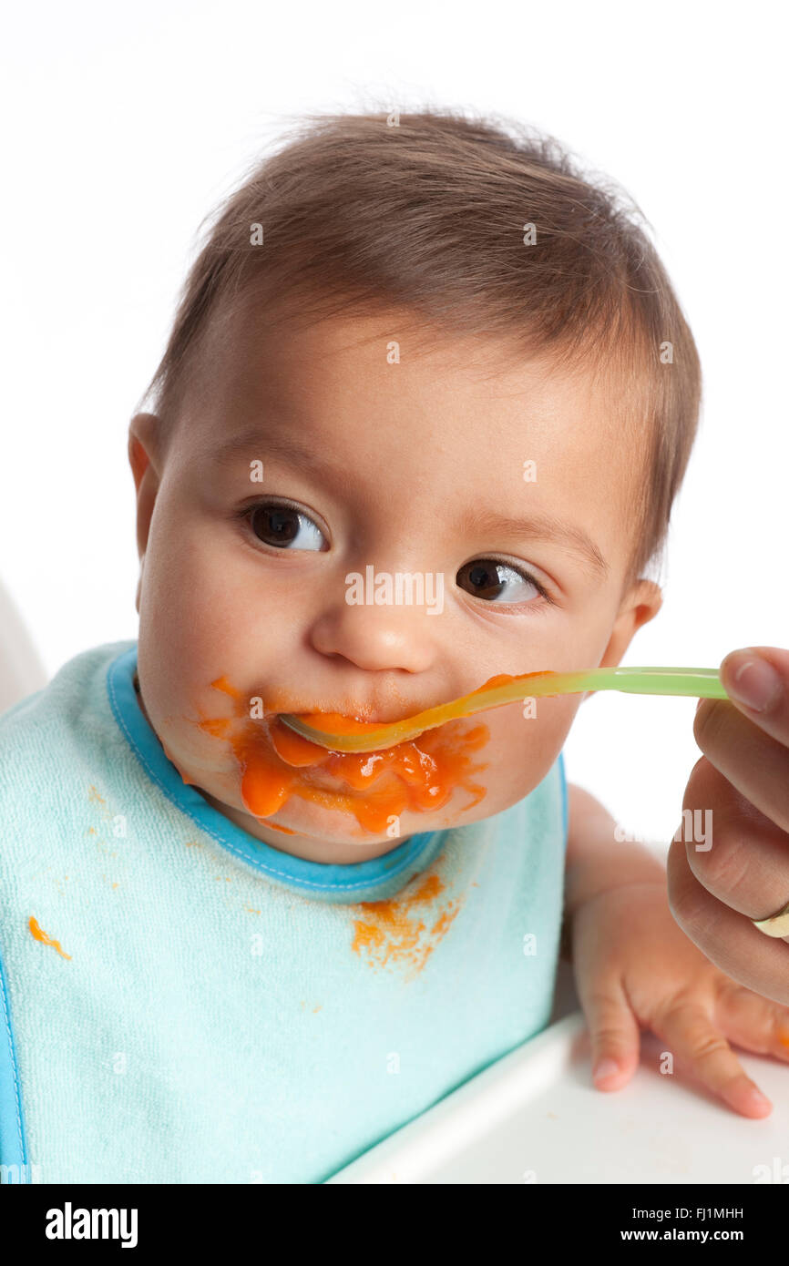 Baby girl è alimentato le carote con un cucchiaio su sfondo bianco Foto Stock