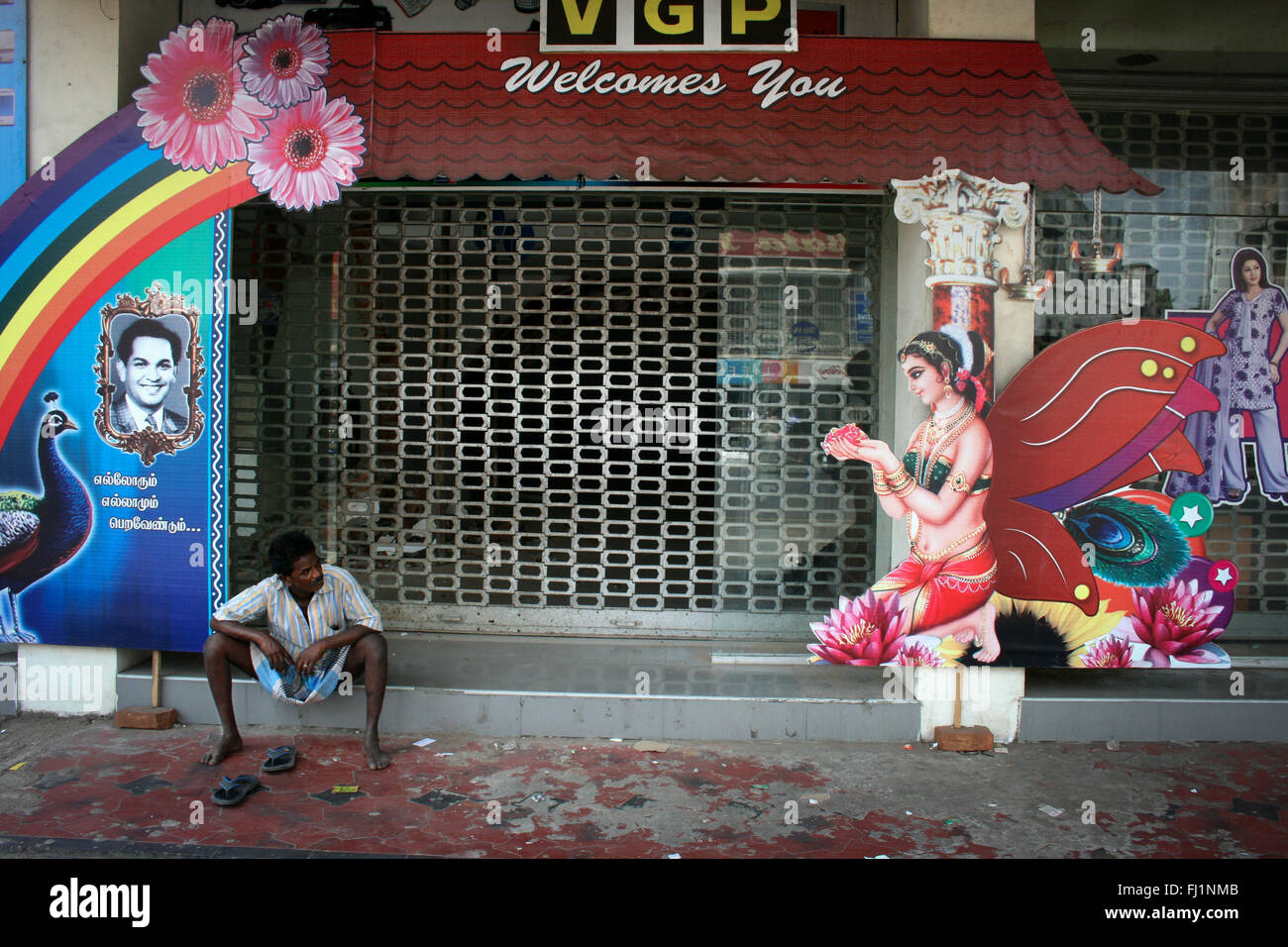Uomo seduto da solo sulla strada guardando il segno che rappresenta una bella donna o dea o angel in una strada di Chennai, India Foto Stock