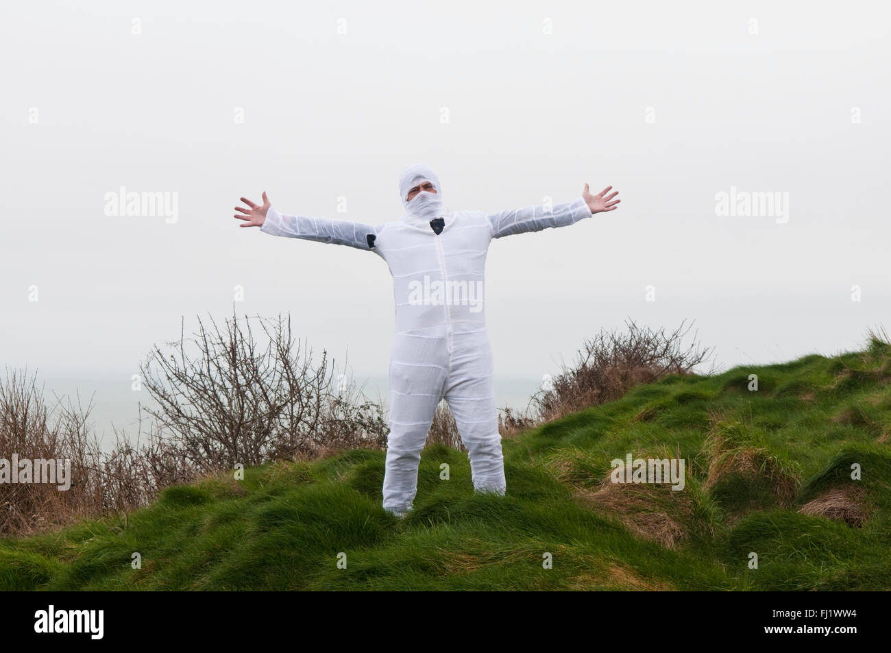 Uomo in una tenuta bianco tuta caldaia con la sua testa in bende di bianco in piedi in un campo con braccia aperte Foto Stock