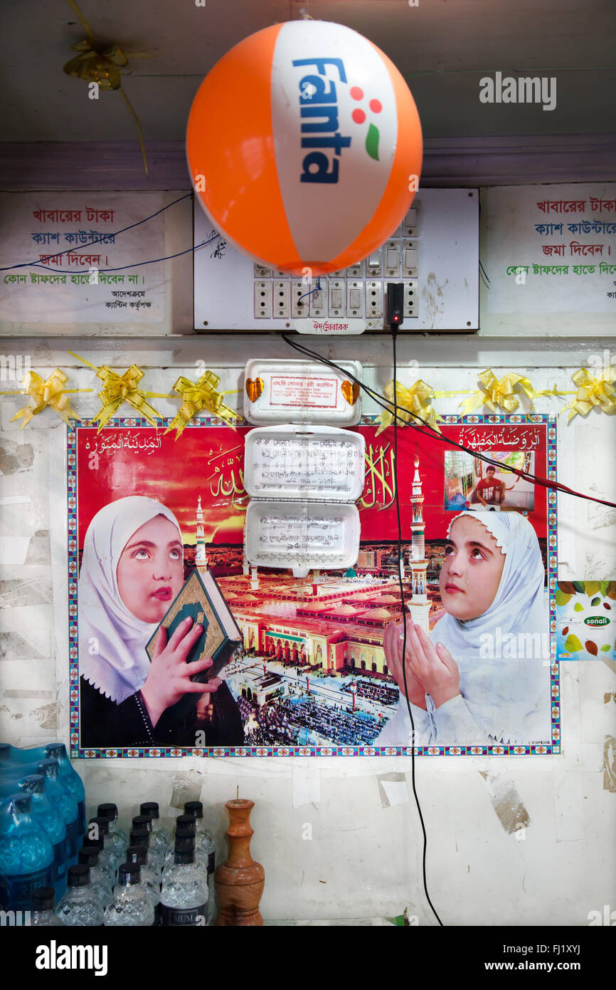 Islamico tipica decorazione interna con l'immagine di due ragazze musulmane pregando e appicture della Mecca e Fanta palloncino, in un negozio in Bangladesh Foto Stock