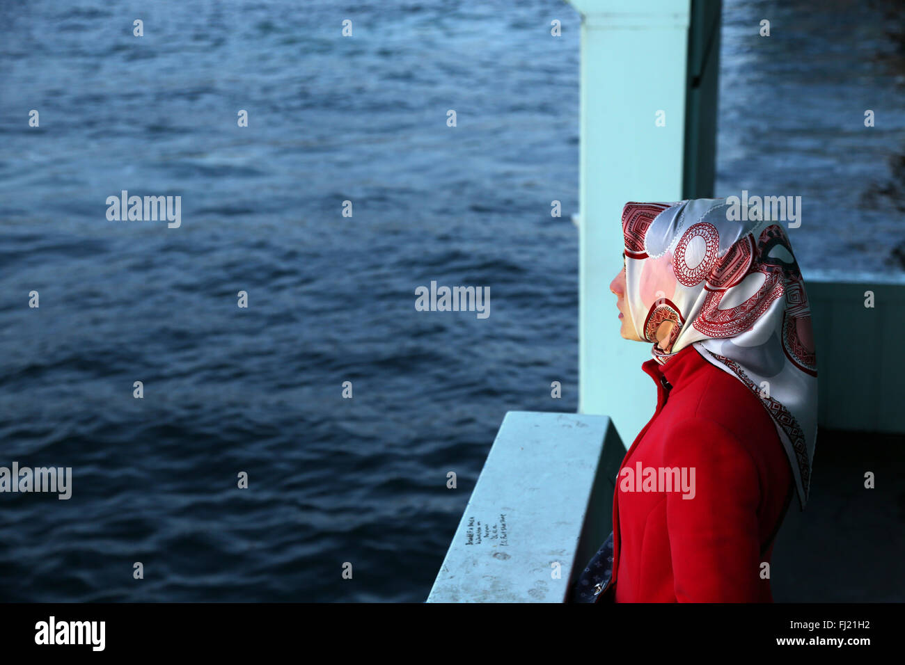 Un solitario donna musulmana guarda al fiume sul Bosforo dal Ponte di Galata a Istanbul Foto Stock
