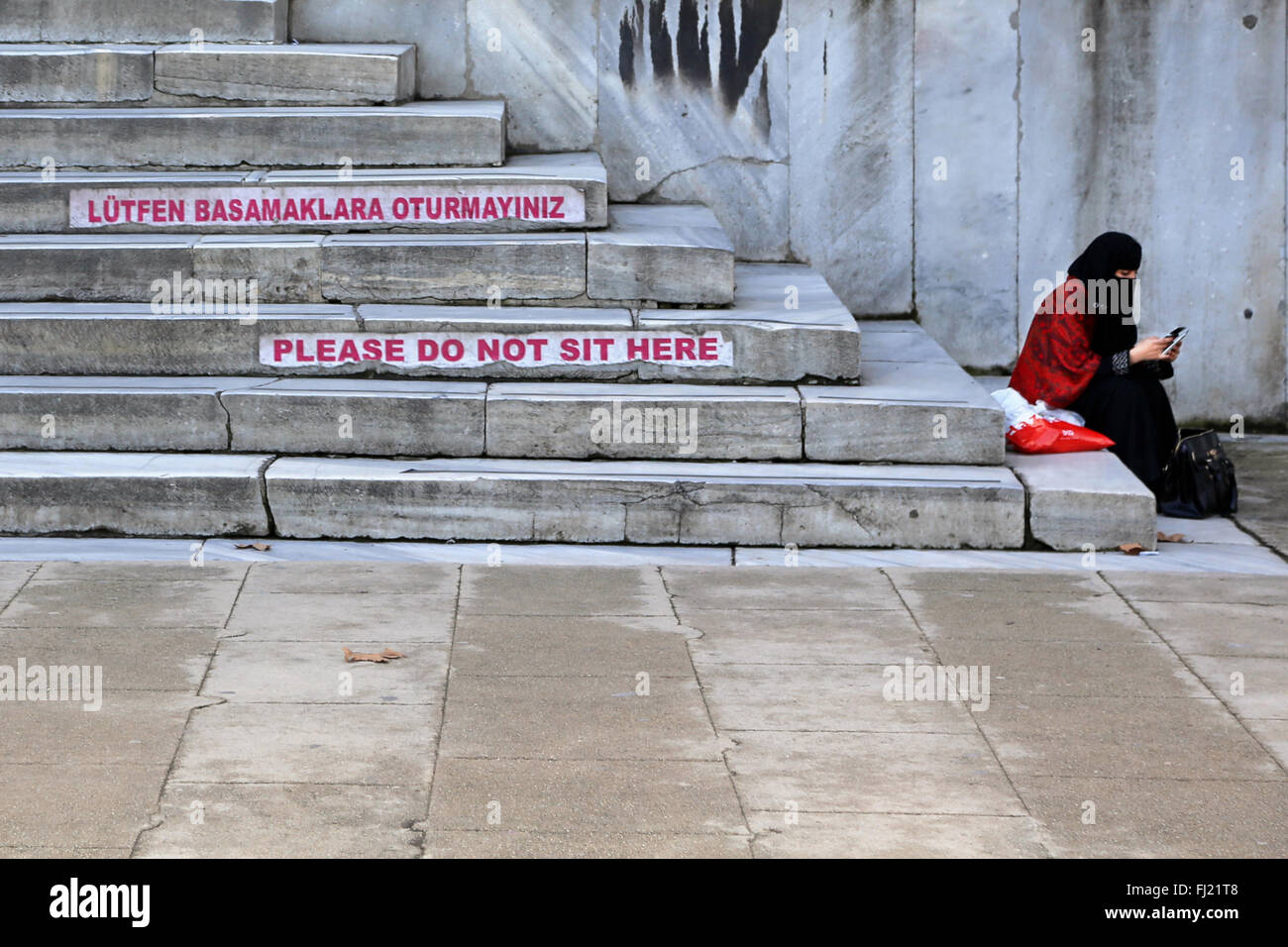Una donna musulmana si siede sui gradini della moschea blu con "Si prega di non sedersi qui' segno , Istanbul Foto Stock
