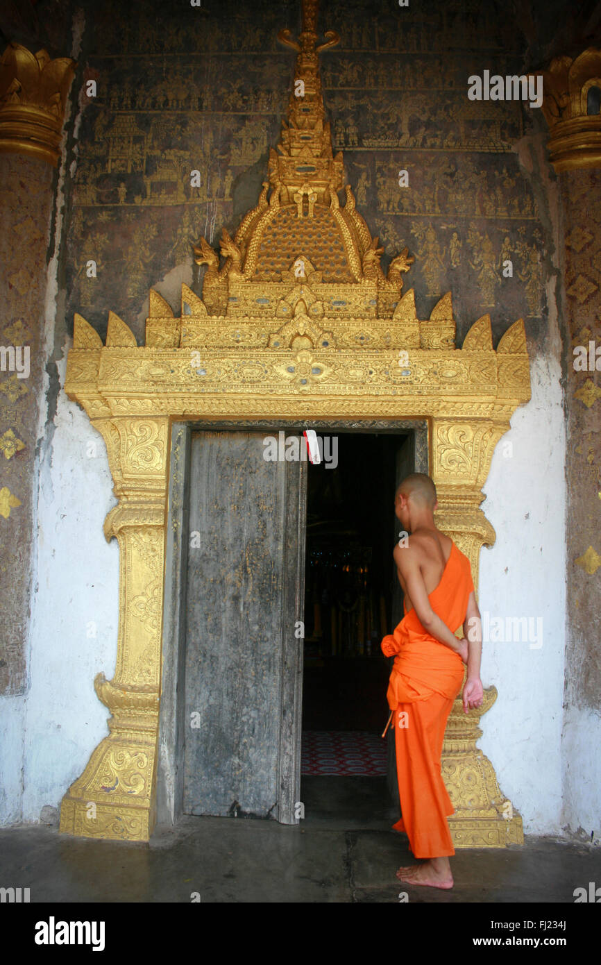 Monaco buddista di fronte a una porta all'ingresso del tempio a Luang Prabang, Laos, Asia Foto Stock