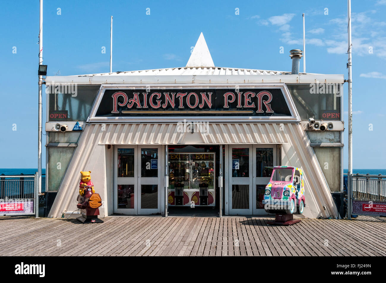 La luce diretta del sole sottolinea i bambini passeggiate al di fuori di un grande padiglione di alloggiamento di una sala giochi situato sul molo di Paignton Foto Stock