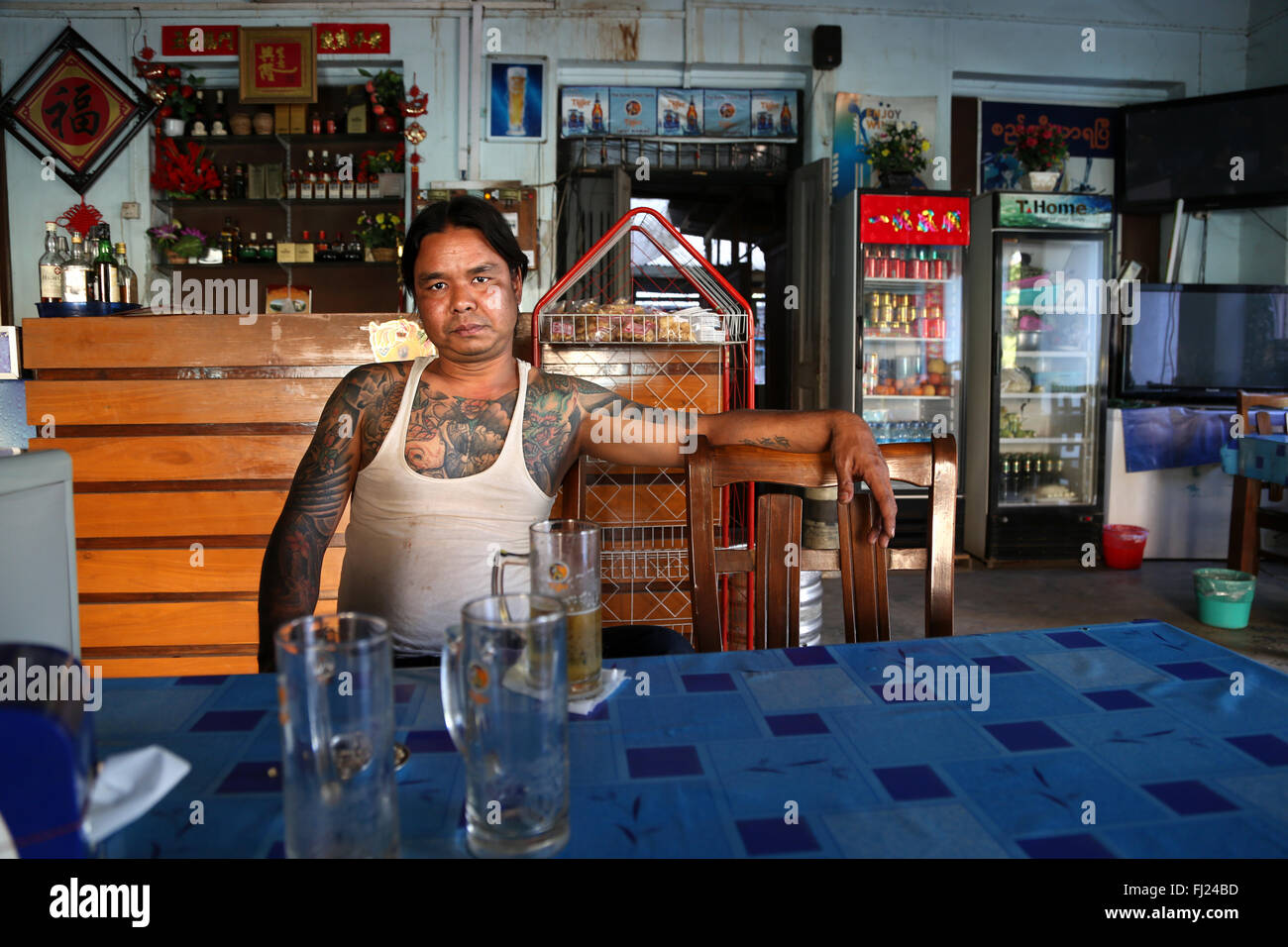 Uomo birmano con tatuaggi seduto da solo in ristorante a Mandalay, Myanmar Foto Stock
