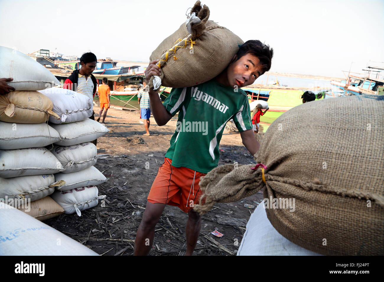 Lavoratore che trasportano pesanti sacco di iuta a Bagan, Myanmar, con 'Myanmar' t shirt Foto Stock