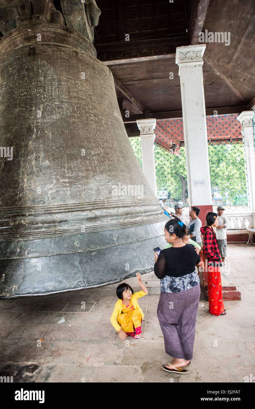Paviglione di bronzo massiccio della campana di Mingun Mingun Myanmar | MINGUN, Myanmar — Un bambino allunga la mano per toccare il bordo della campana di Mingun, il cui diametro di 16 piedi (4,9 m) fa apparire piccoli i visitatori che vi stanno sotto. Commissionata dal re Bodawpaya per il suo stupa incompiuto e fusa intorno al 1808–1810, la campana di bronzo di circa 90 tonnellate è alta 12 piedi (3,7 m) ed è ampiamente considerata la più grande campana suonante del mondo. Foto Stock