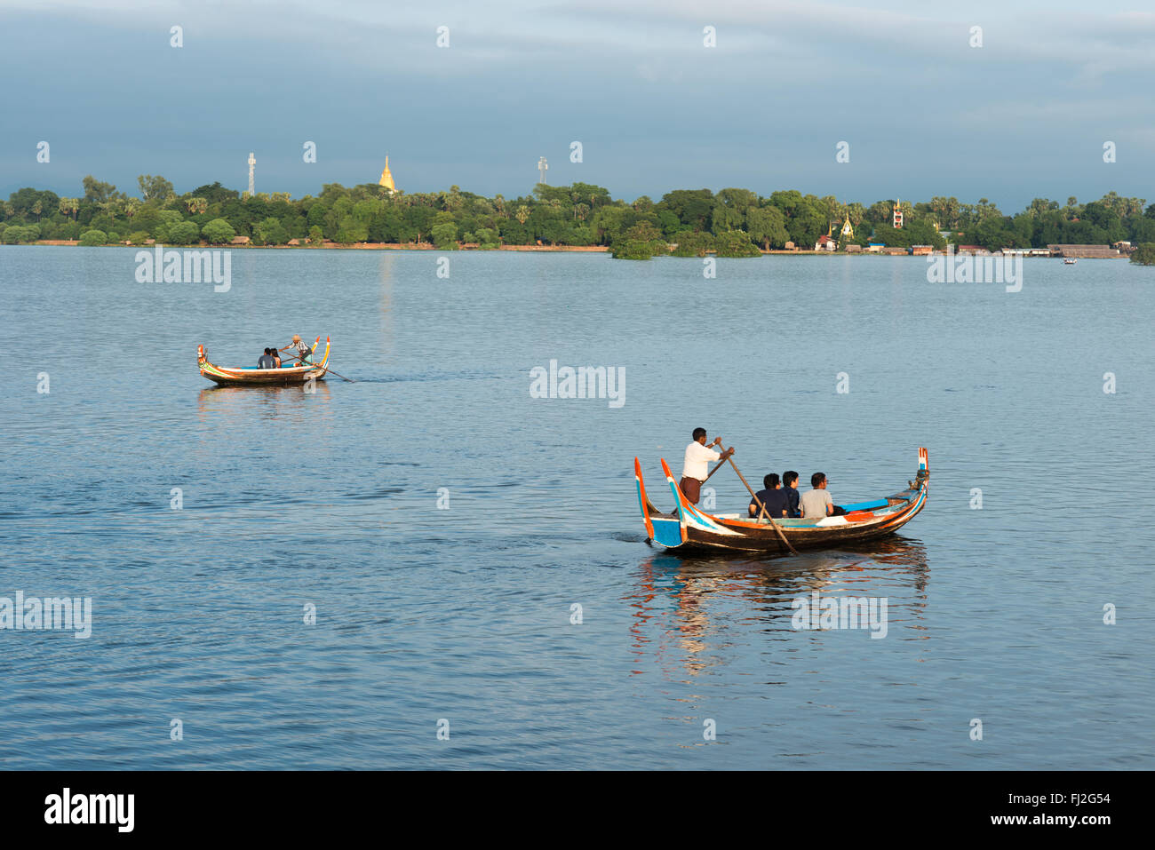 Lago Taungthaman barche a remi Amarapura Myanmar // LAGO TAUNGTHAMAN, Myanmar - piccole barche a remi in legno trasportano i turisti attraverso il lago al tramonto vicino al famoso Ponte U Bein. Il lago Taungthaman nella città di Amarapura è un corpo idrico stagionale situato 11 chilometri a sud-ovest di Mandalay che ha guadagnato importanza durante la dinastia Konbaung (1752-1885). Il lago si collega al sistema fluviale Ayeyarwady ed è attraversato dal ponte U Bein di 1,2 chilometri, costruito tra il 1849-1851 utilizzando teak recuperato dal Palazzo Inwa smantellato. Il vicino monastero di Mahagandayon, fondato nel 1908, ospita oltre 1.300 metri Foto Stock