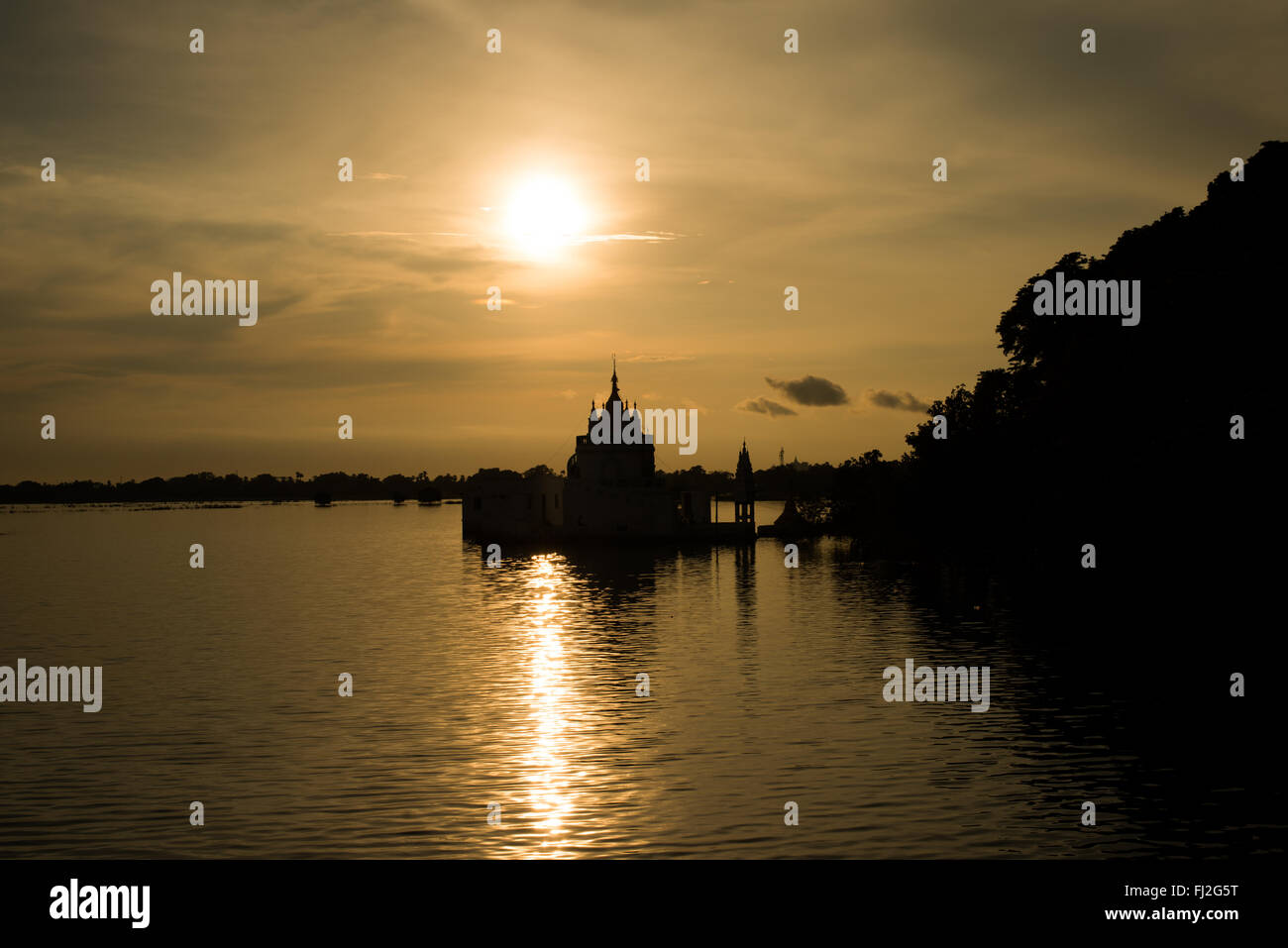 Taungthaman Lake Pagoda silhouette Mandalay Myanmar // TAUNGTHAMAN Lake, Myanmar — Una sagoma di pagoda si estende nel lago Taungthaman vicino a Mandalay, uno dei corpi idrici culturalmente più significativi del Myanmar centrale. Il lago guadagnò importanza durante la dinastia Konbaung (1752-1885) quando divenne strategicamente posizionato tra le mutevoli capitali reali del Myanmar. Situato a 11 chilometri a sud-ovest di Mandalay nella cittadina di Amarapura, questo lago stagionale si collega al sistema fluviale Ayeyarwady e ospita il famoso ponte U Bein, di 1,2 chilometri. L'area funge da centro vitale per i Buddha Foto Stock