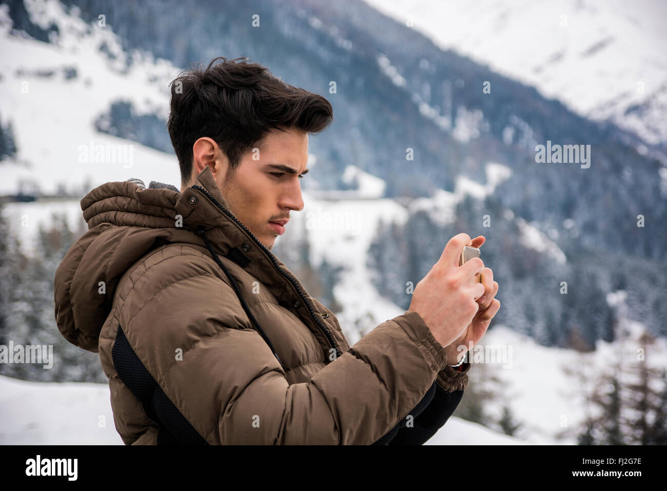 Vista laterale sui capelli scuri giovane cappotti tenendo fotografia di paesaggio in montagna con lo smartphone Foto Stock