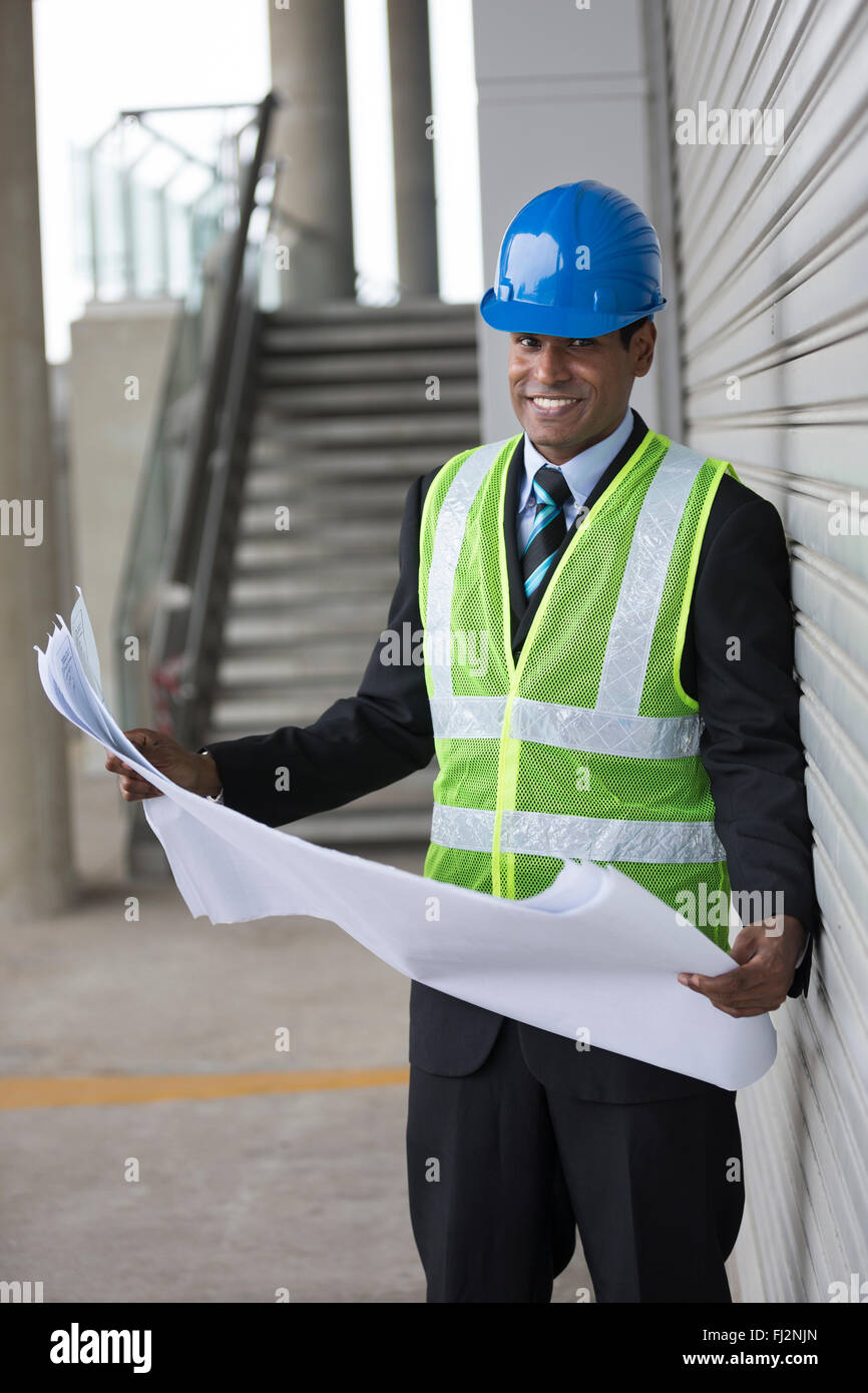 Ritratto di un maschio indiano ingegnere industriale al lavoro tenendo premuto il disegno tecnico piani. Foto Stock