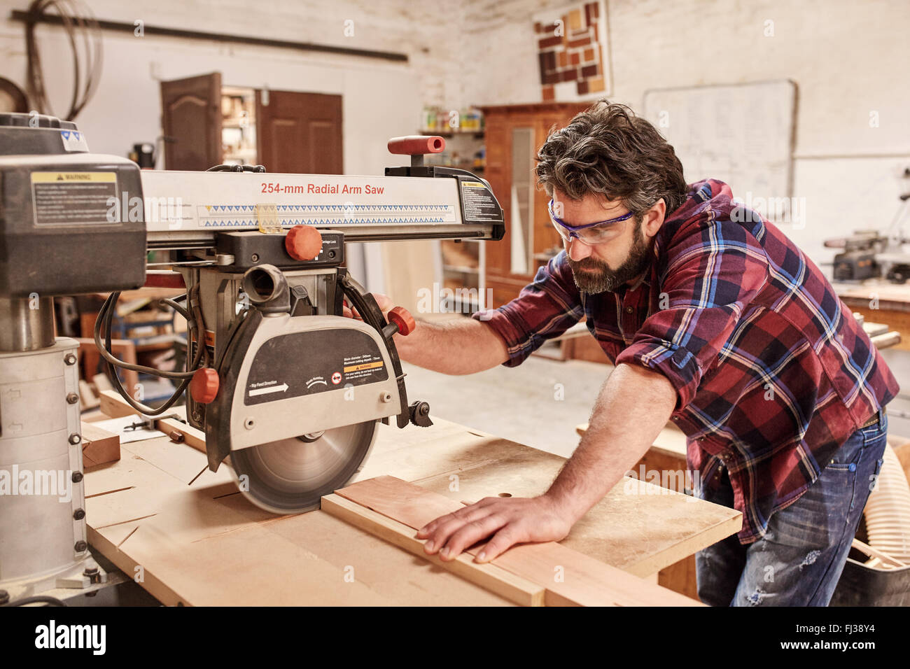 Carpenter utilizzando il braccio radiale sega per tagliare il legno in officina Foto Stock