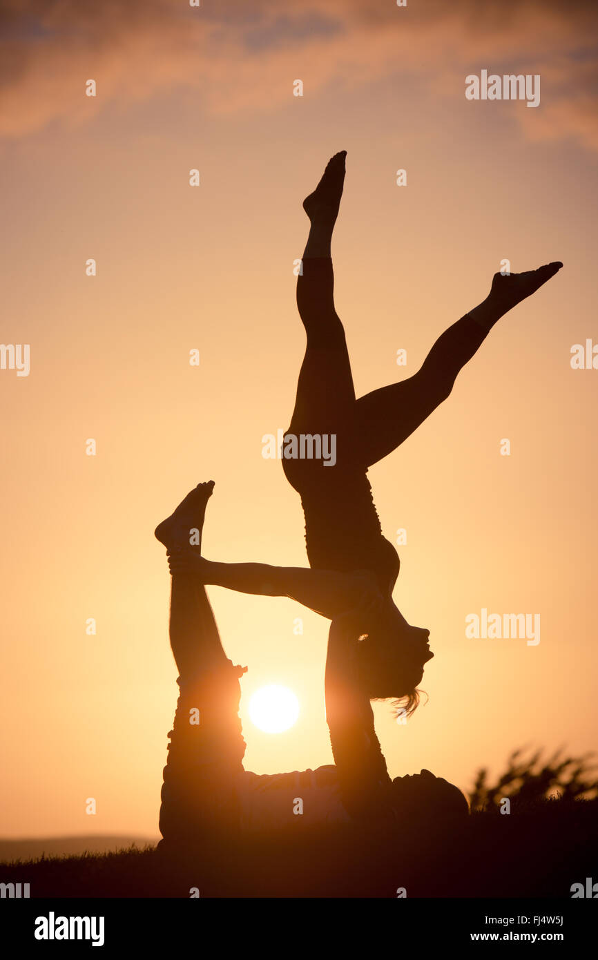 Silhouttes esecuzione di acro yoga al tramonto Foto Stock