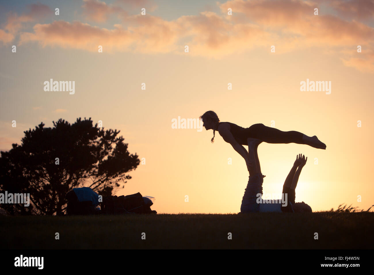 Silhouttes esecuzione di acro yoga al tramonto Foto Stock