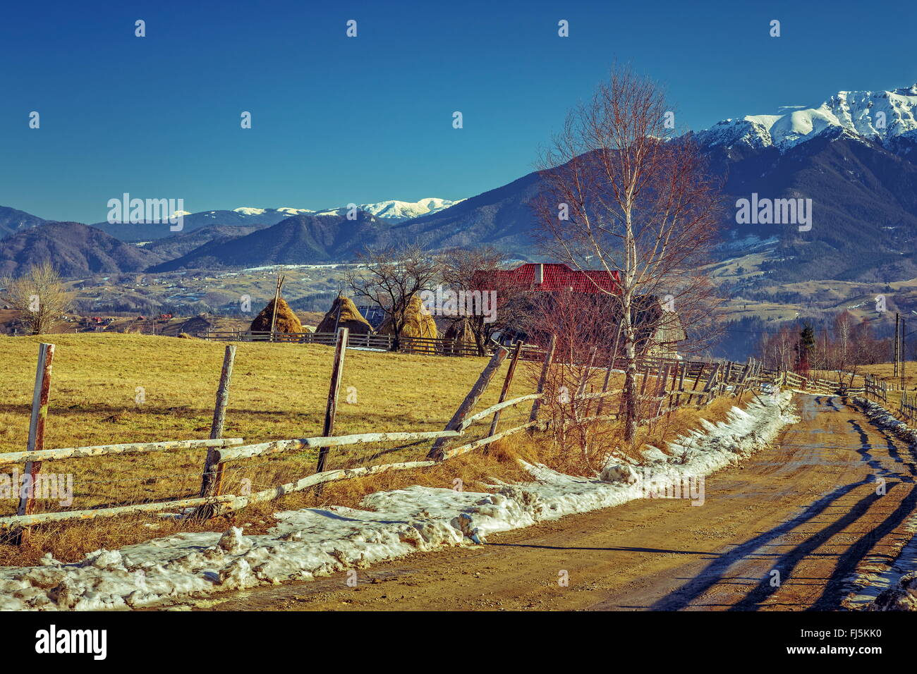 Montagna paesaggio rurale con tradizionale Rumena farm e fangoso country road durante l'inverno nelle valli delle montagne di Bucegi, B Foto Stock