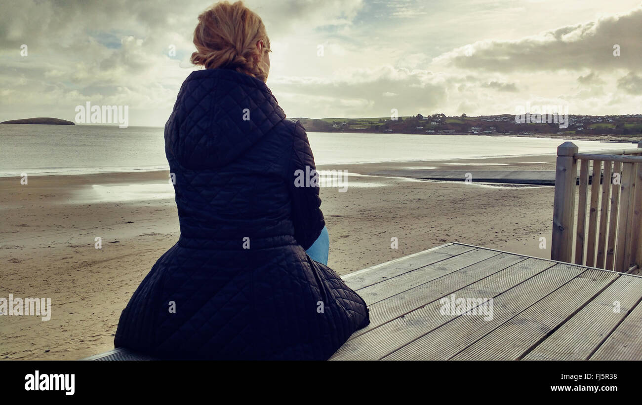 Giovane ed elegante donna seduta in legno sulla spiaggia Foto Stock