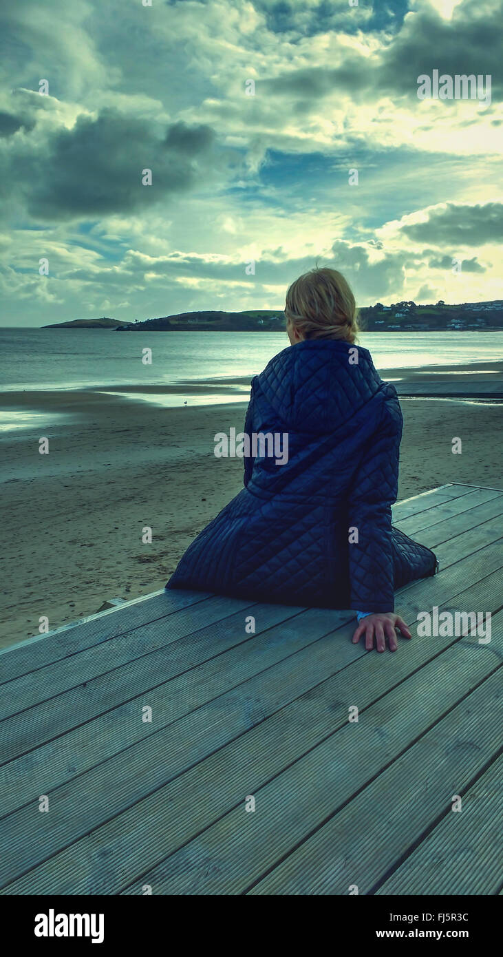 Giovane donna seduta in legno sulla spiaggia Foto Stock