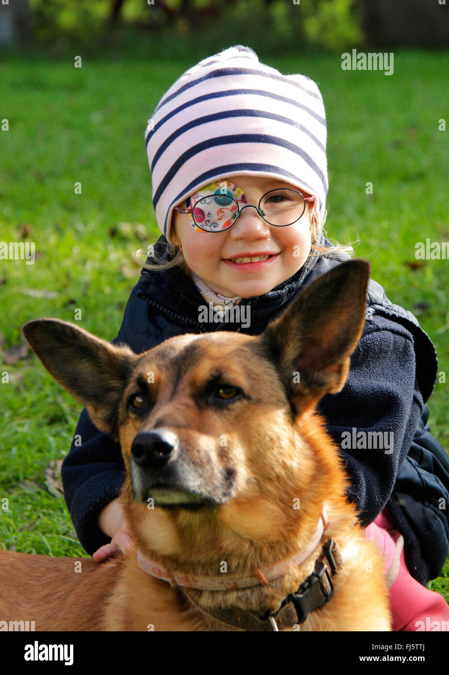 Razza cane (Canis lupus f. familiaris), bambina con occhio patch accarezzare un cane, Germania Foto Stock
