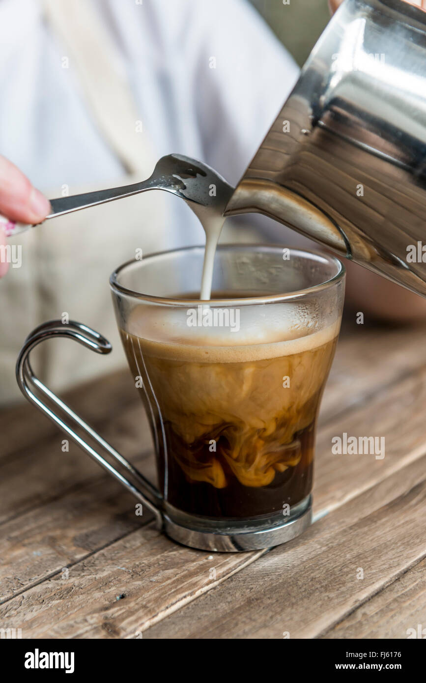 Un caffè nero. Il latte che viene versato in un caffè da un barista. Foto Stock